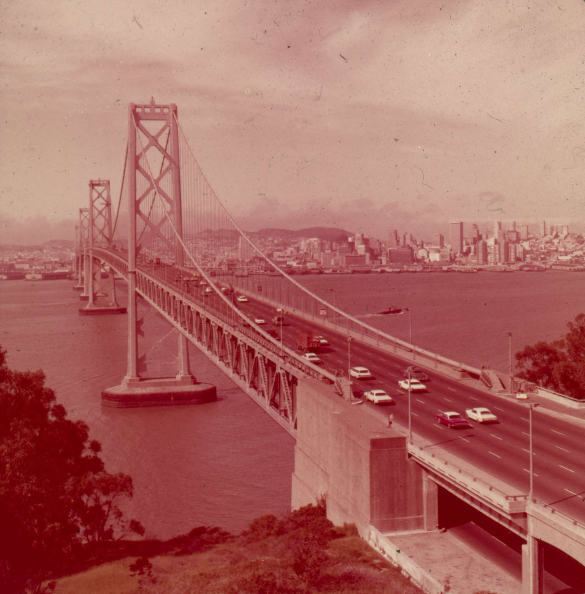 An old photo of the San Francisco-Oakland Bay Bridge with a strong red cast.